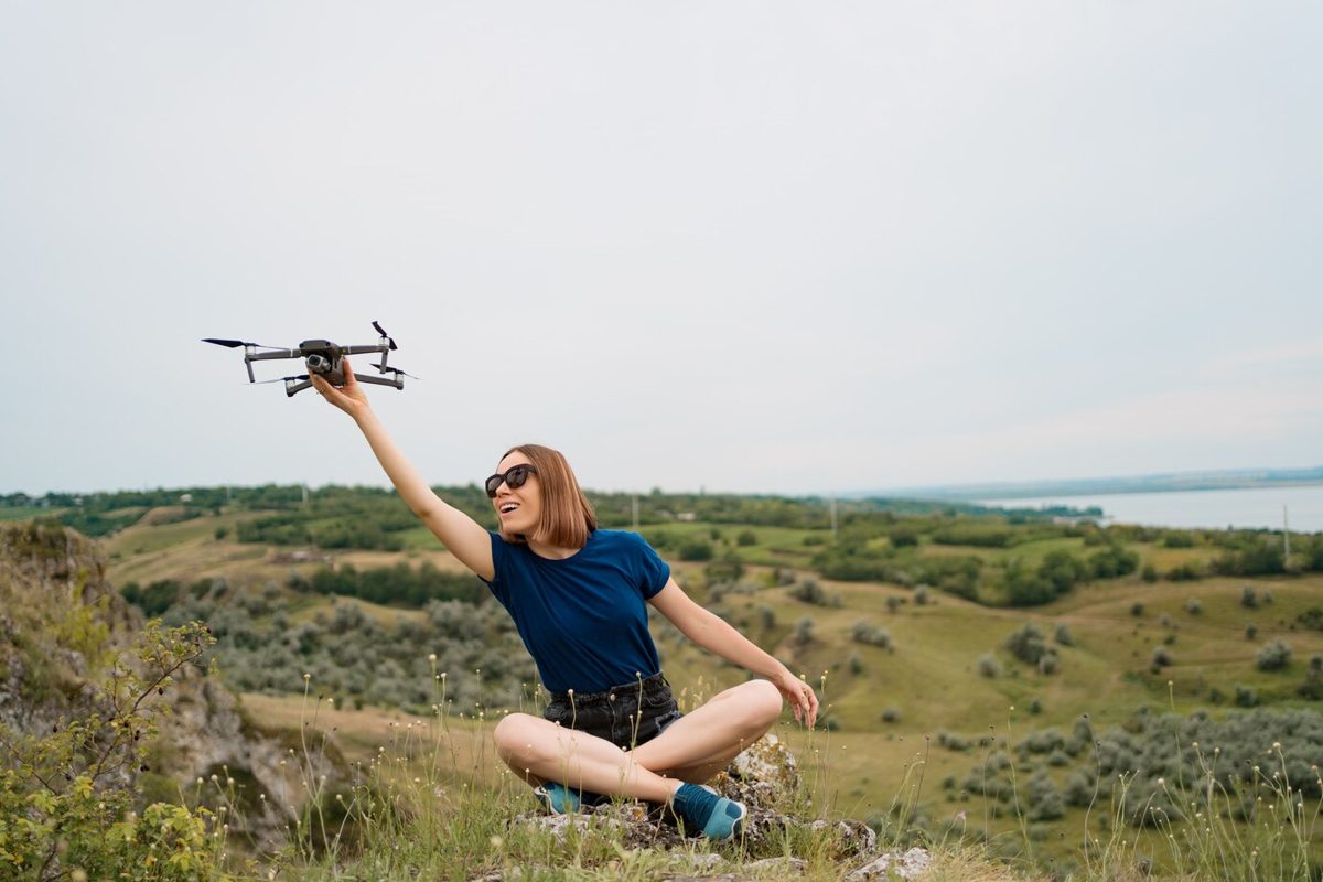 Woman holding a drone while sitting on a green hill