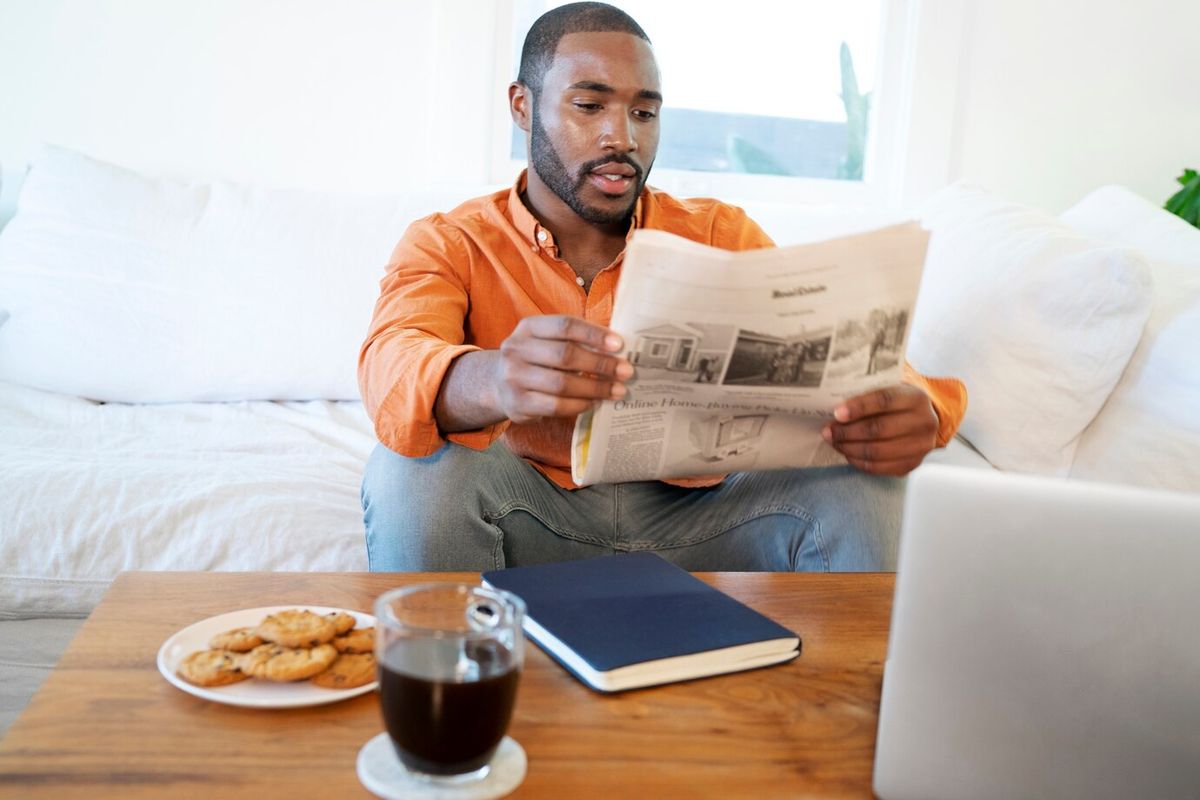 Young man reading a newspaper at home while having coffee