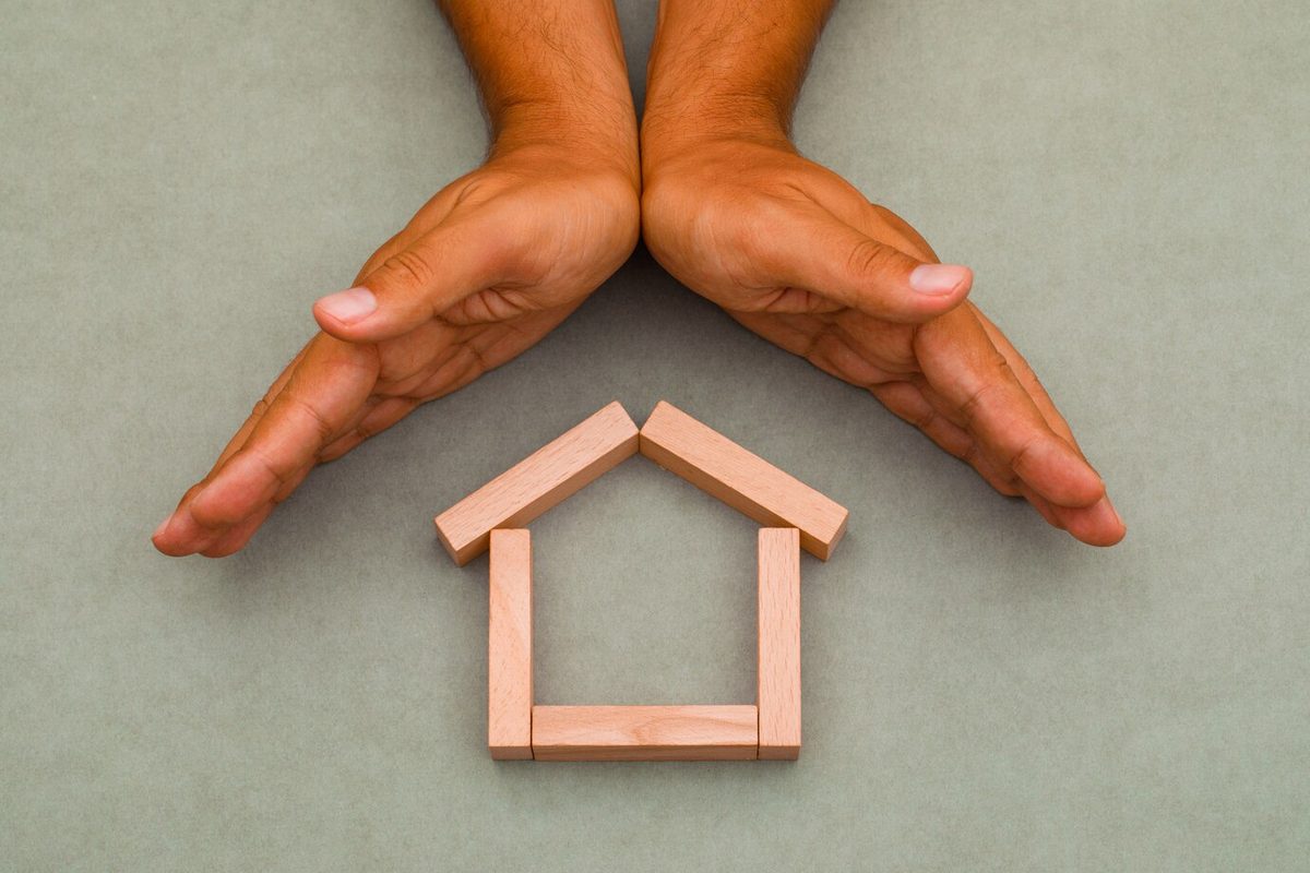 Hands enclosing a small wooden house
