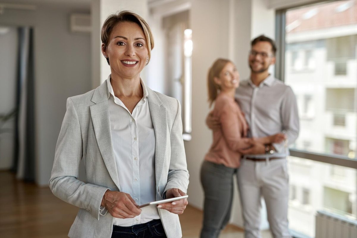 Female real estate agent smiling with a happy couple in the background
